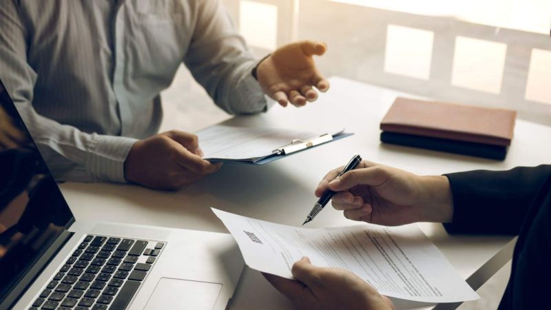 two people sitting at a table with papers and a laptop