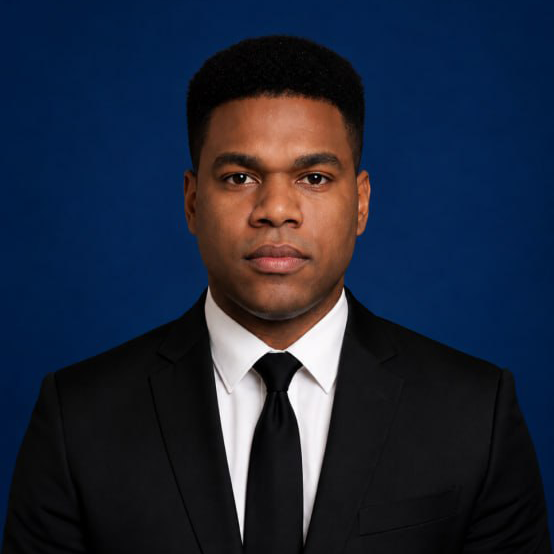 A person in a suit in an office setting, with a confident expression, facing forward.